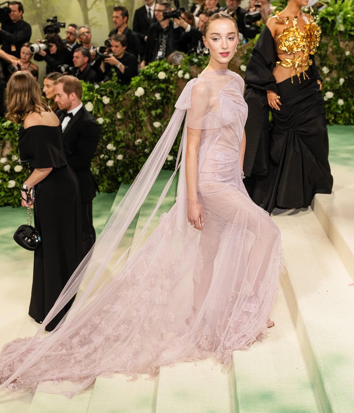 Phoebe Dynevor wears a custom lavender tulle gown by Victoria Beckham with floral embroidery and a cathedral-length train, debuting her engagement ring at the 2024 Met Gala