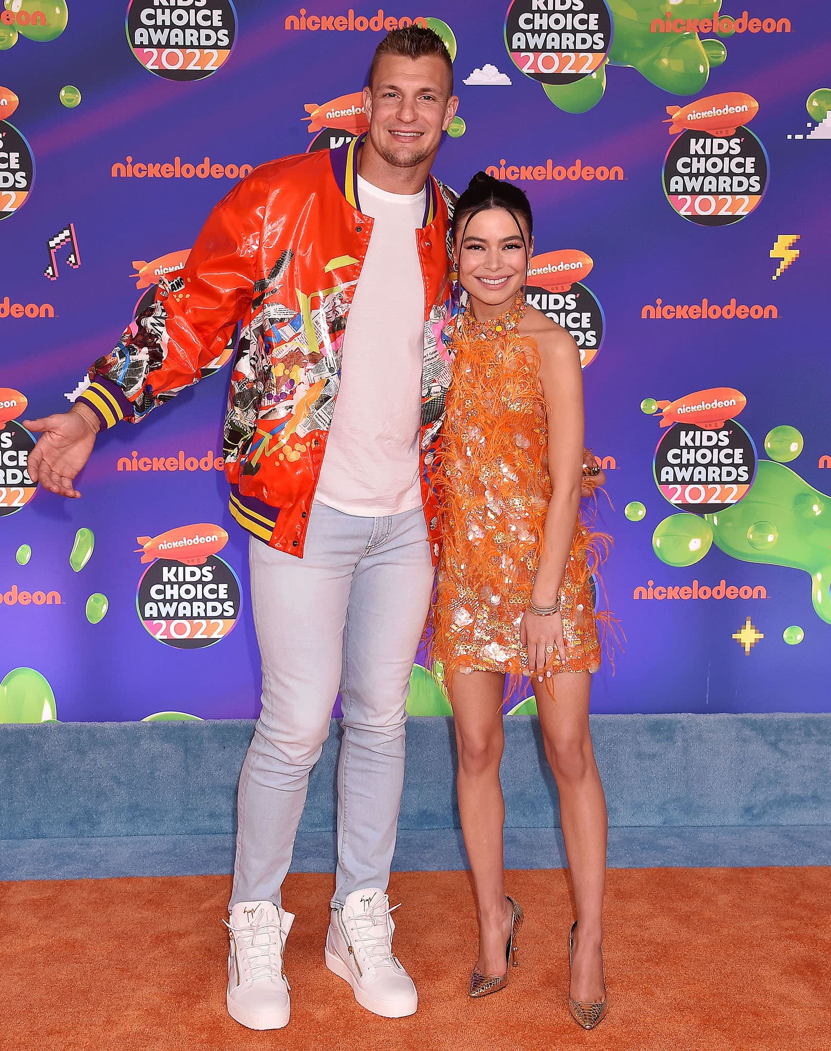 Kids Choice Awards 2022 hosts Rob Gronkowski and Miranda Cosgrove pose together on the orange carpet