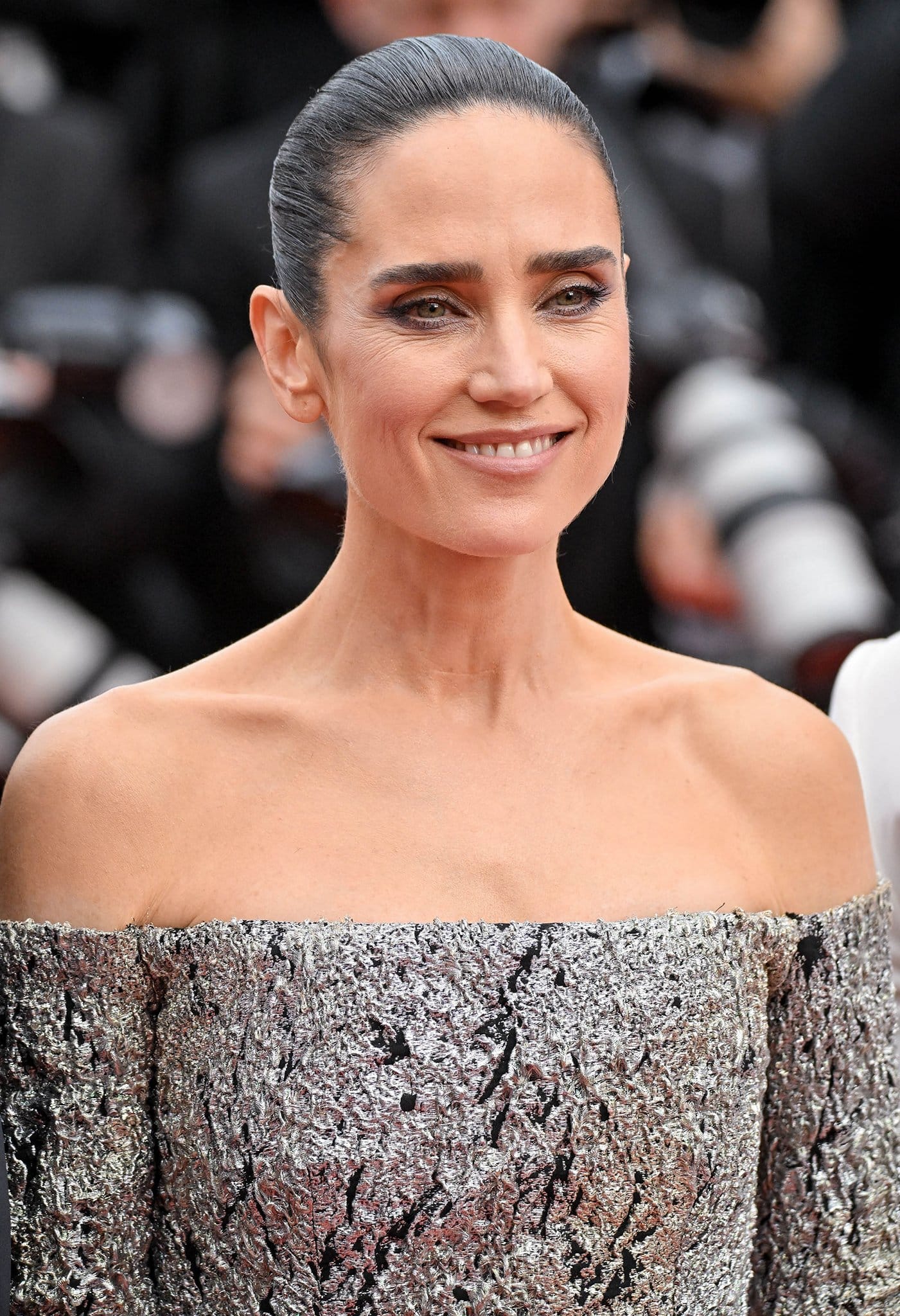 Jennifer Connelly wears a slicked back bun with subtle smokey eyeshadow and nude lipstick