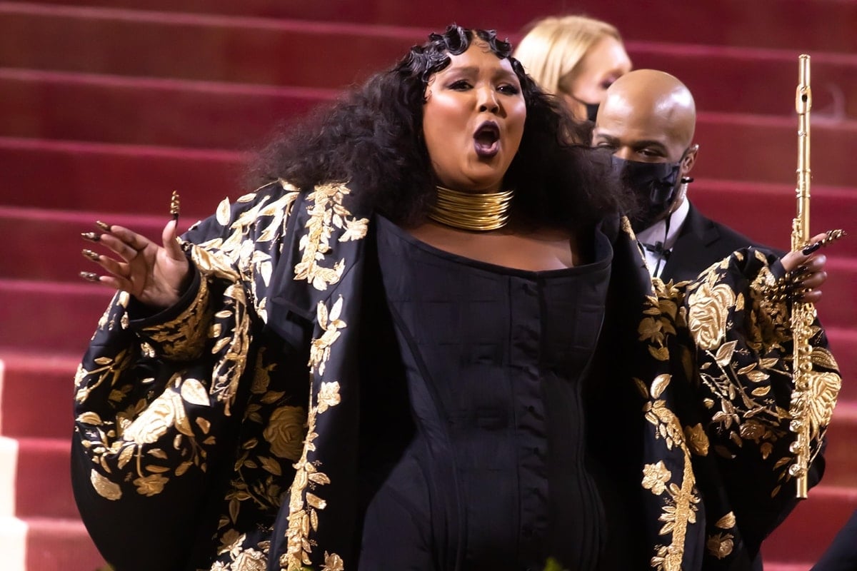 Lizzo shows off her long nails, gold choker necklace by Lorraine West, and gold flute