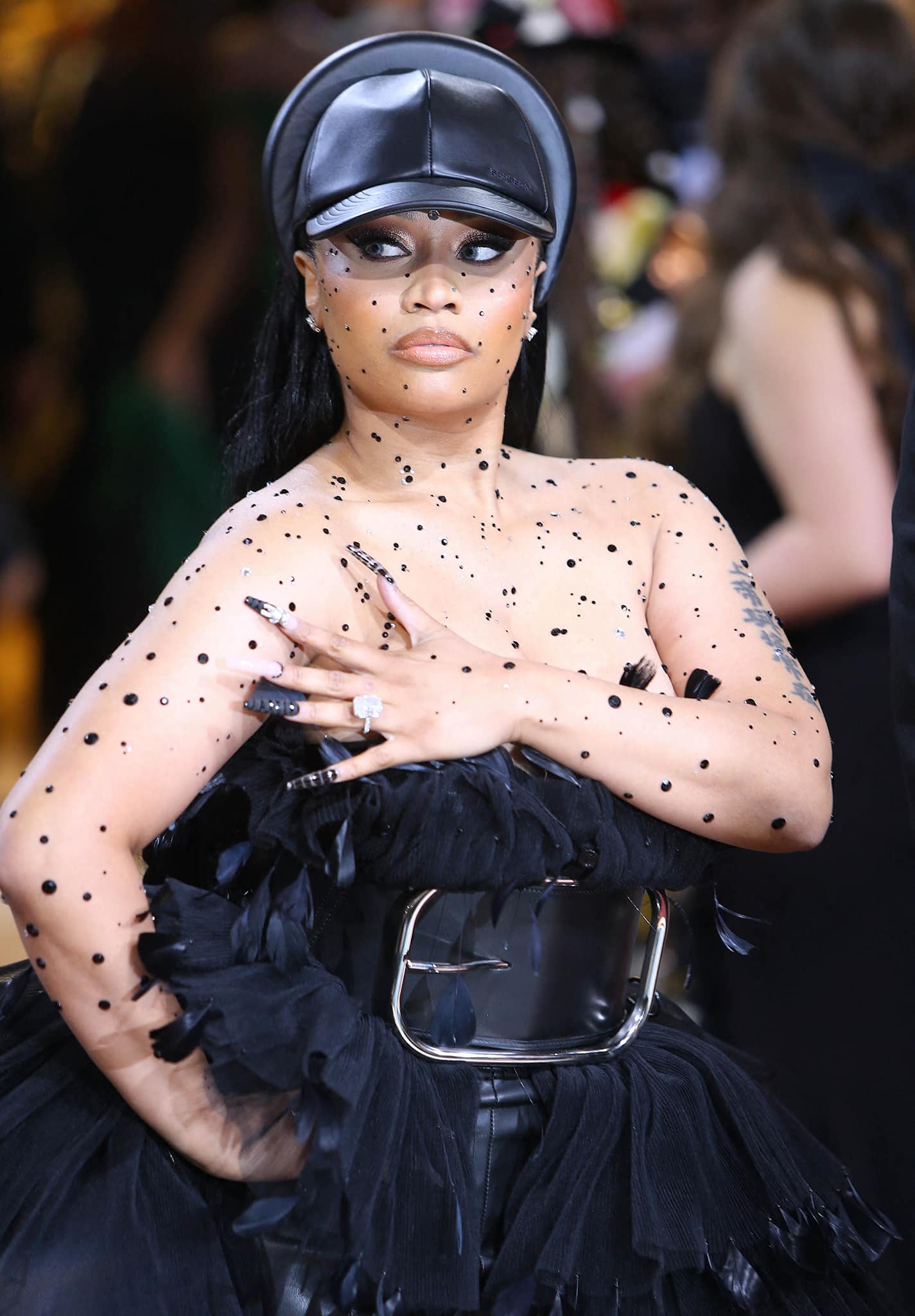Nicki Minaj teams her outfit with a leather baseball cap and wears bronze smokey eyeshadow, thick winged eyeliner, peachy blush, and matching lipstick