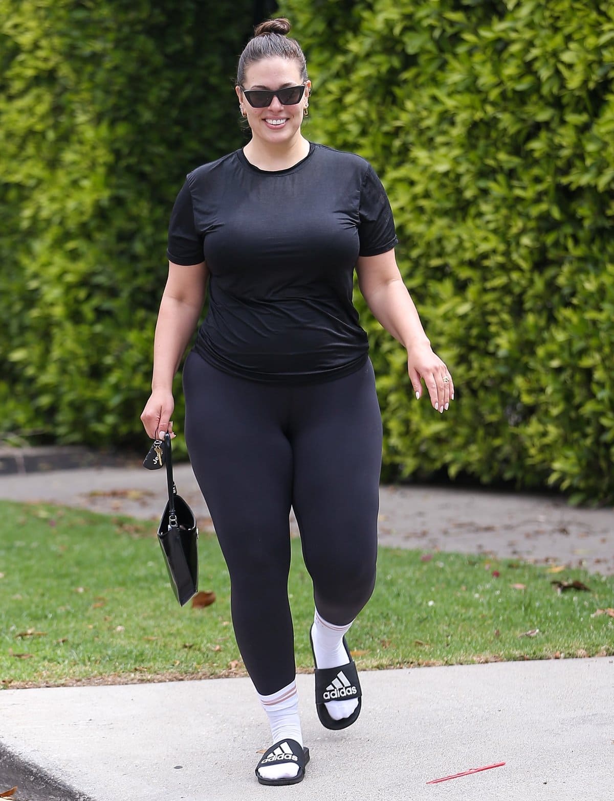 Ashley Graham leaves a Pilates class in black leggings, white socks, and Adidas slides