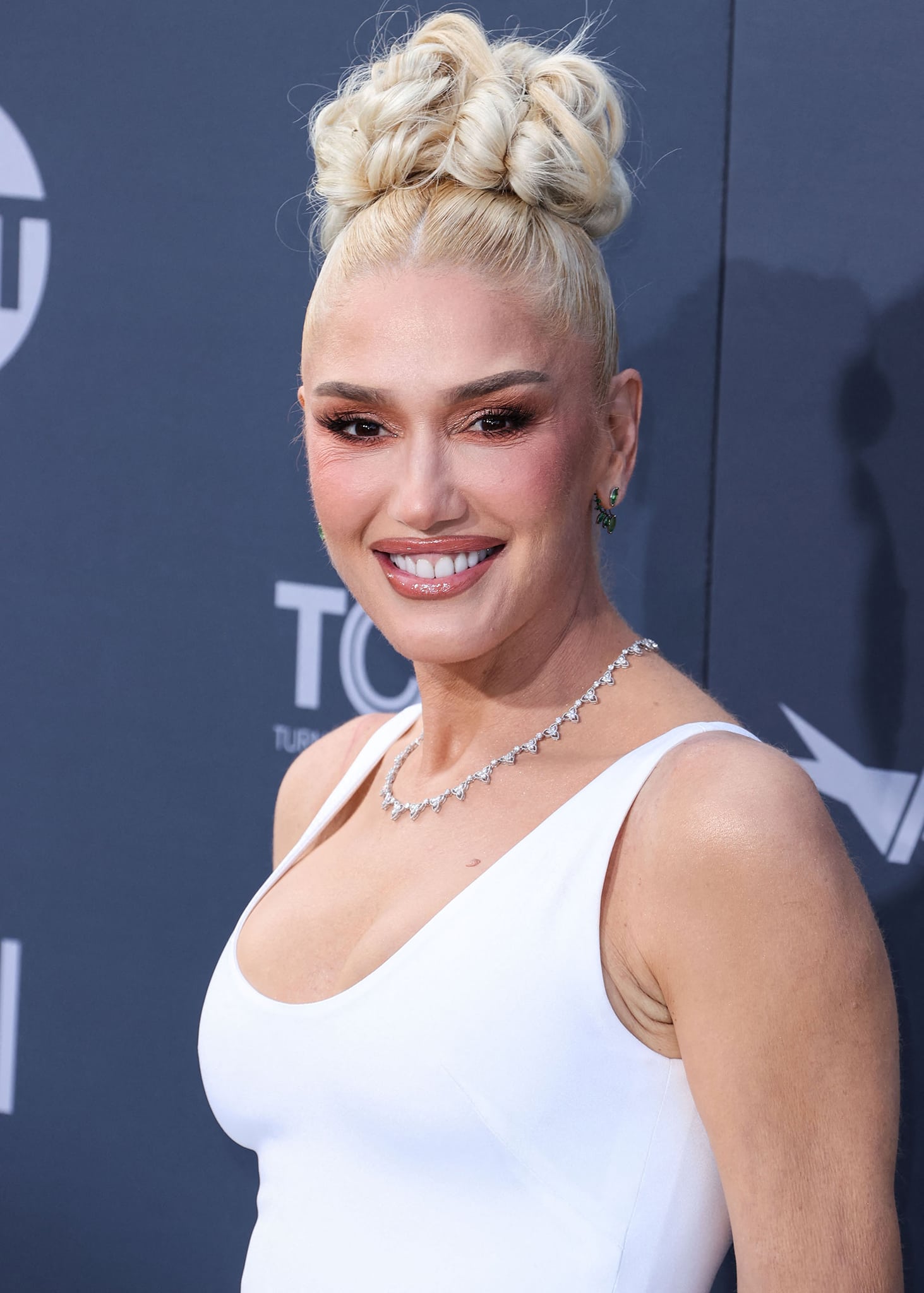 Gwen Stefani pulls her tresses up into a curled high bun and wears pink smokey eyeshadow with neutral lip gloss