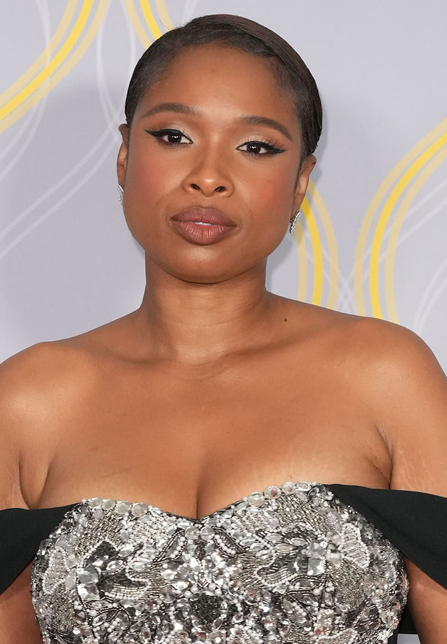 Jennifer Hudson styles her short hair sleek and wears winged eyeliner with brown lipstick, bronzer, and pinkish eyeshadow