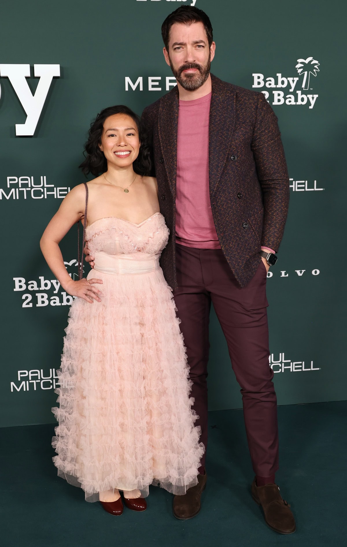 Linda Phan pairs glossy burgundy heels with a whimsical blush pink ruffled gown, while Drew Scott complements her look in wine-colored trousers and chocolate brown suede shoes at the 2024 Baby2Baby Gala held at the Pacific Design Center on November 9, 2024, in West Hollywood, California