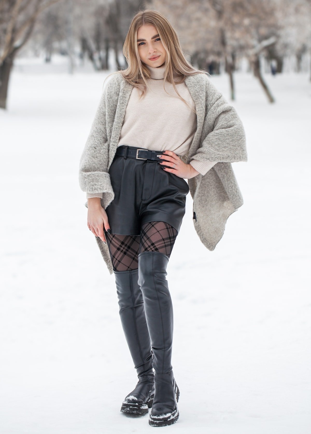 A beautiful young blonde woman shows how to wear black over-the-knee boots in winter