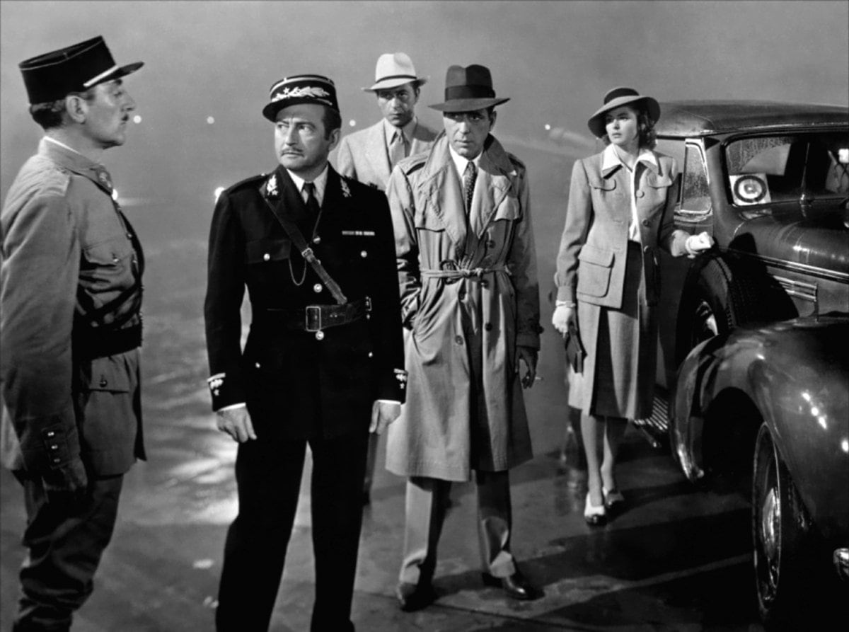 Humphrey Bogart wears a trench coat as Rick Blaine with Ingrid Bergman as Ilsa Lund, Claude Rains as Captain Louis Renault, and Paul Henreid as Victor Laszlo in the 1942 American romantic drama film Casablanca