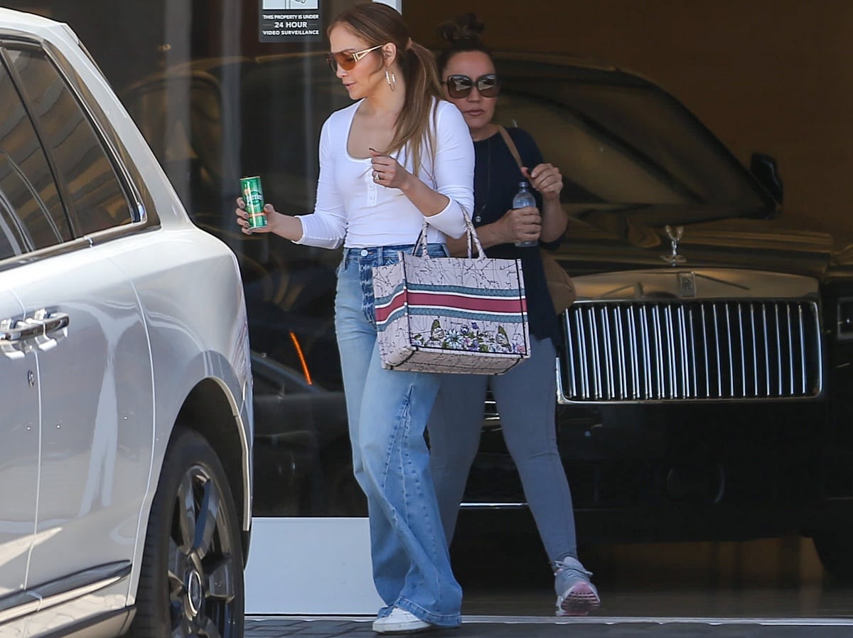 Jennifer Lopez wearing a white Henley, Flare jeans, and Coach sneakers in LA