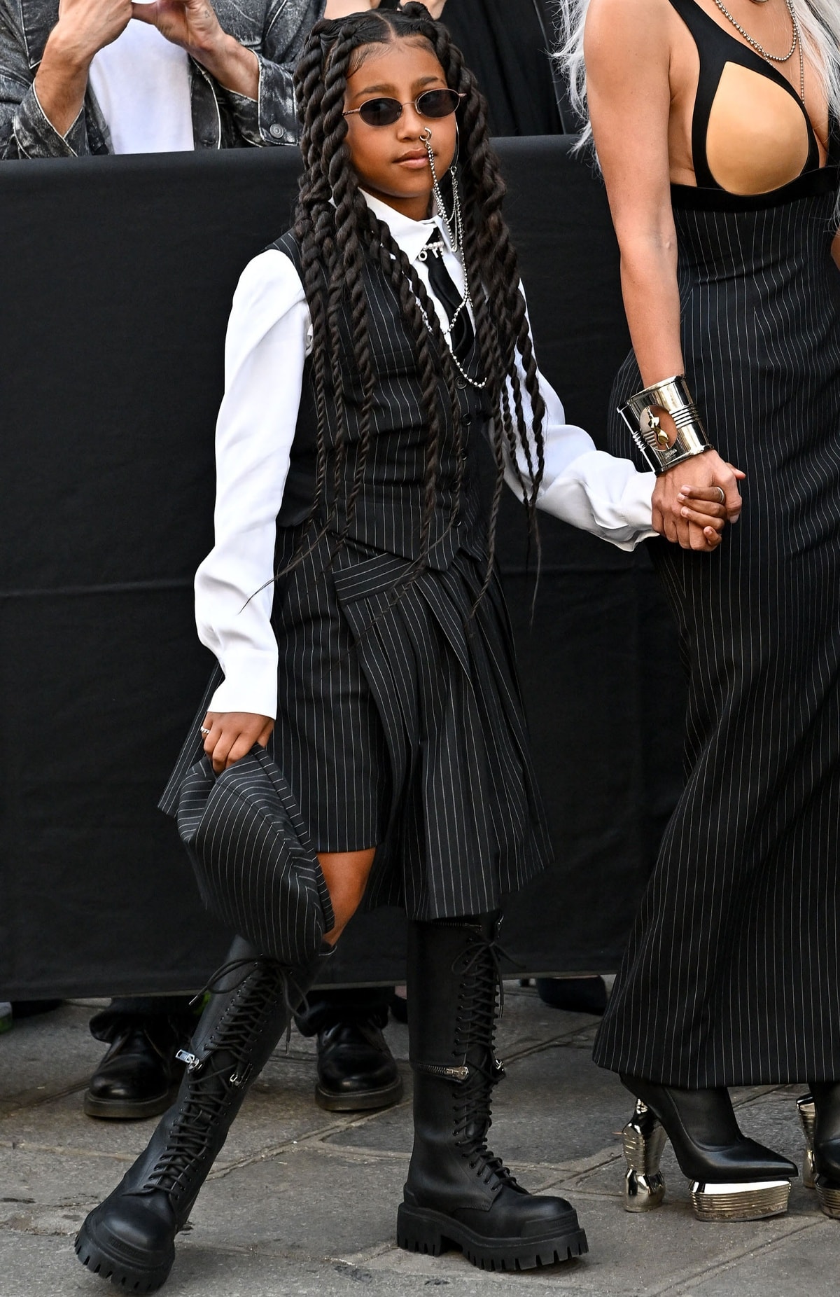 North West wearing a nose ring featuring long, dangling chains with sunglasses, a pinstriped set and black knee-high combat boots
