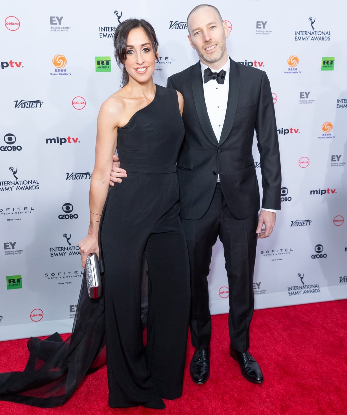 Catherine Reitman exudes elegance in a sleek one-shoulder black jumpsuit with a dramatic sheer train, while her husband, Philip Sternberg, looks dapper in a classic black tuxedo at the 46th Annual International Emmy Awards on November 19, 2018, at the New York Hilton Midtown in New York City