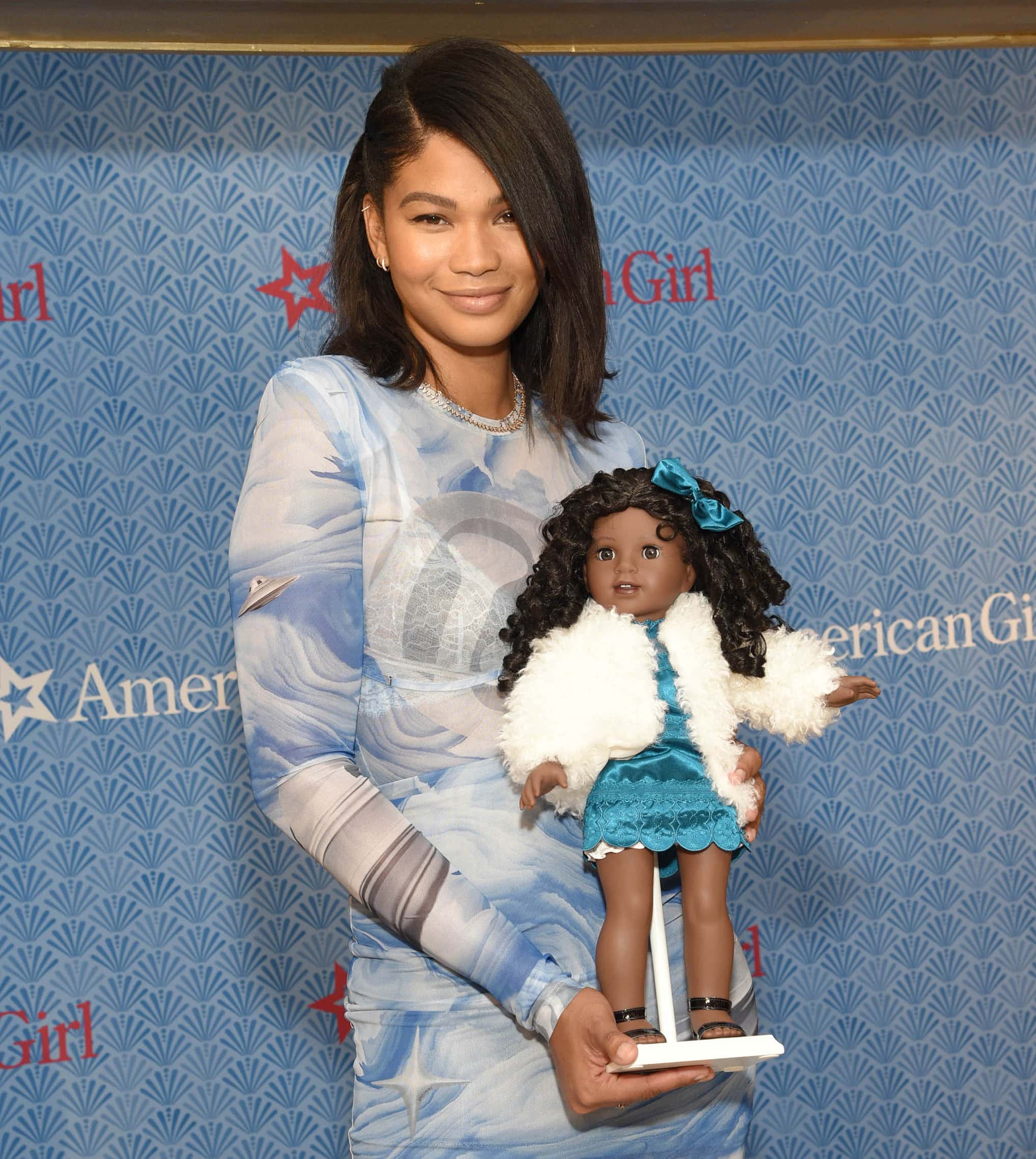 Chanel Iman wears neutral makeup and a deep side part as she carries American Girl's new character Claudie Wells