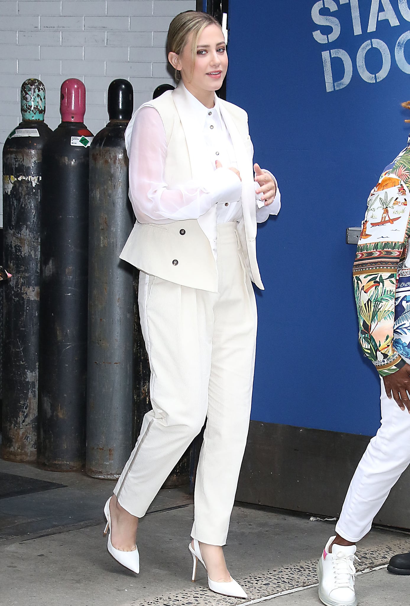 Lili Reinhart looks chic in a white tuxedo suit with a mesh-sleeved blazer and white slingback pumps