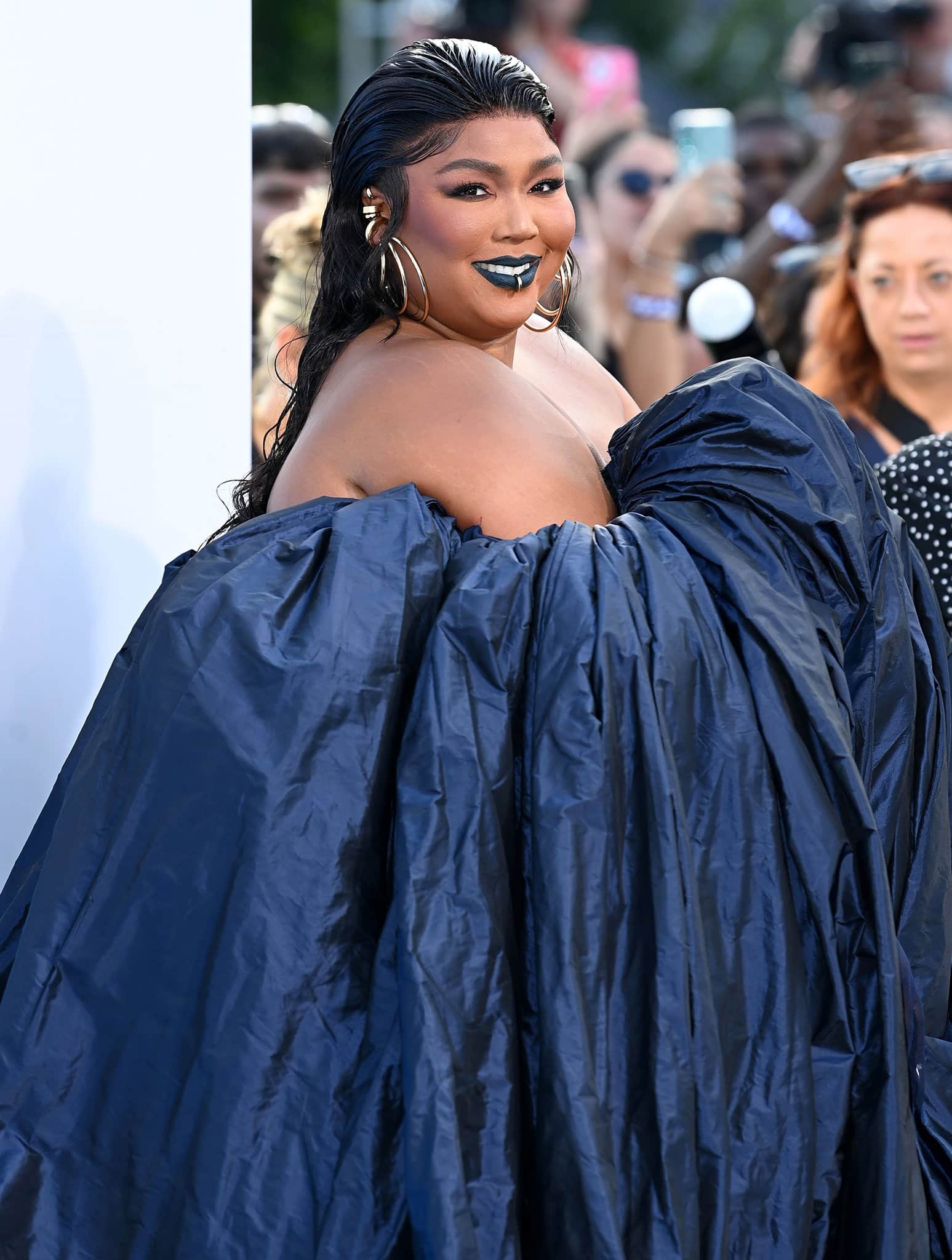 Lizzo adds bling to the look with a lip ring and an array of Jennifer Fisher gold hoop earrings