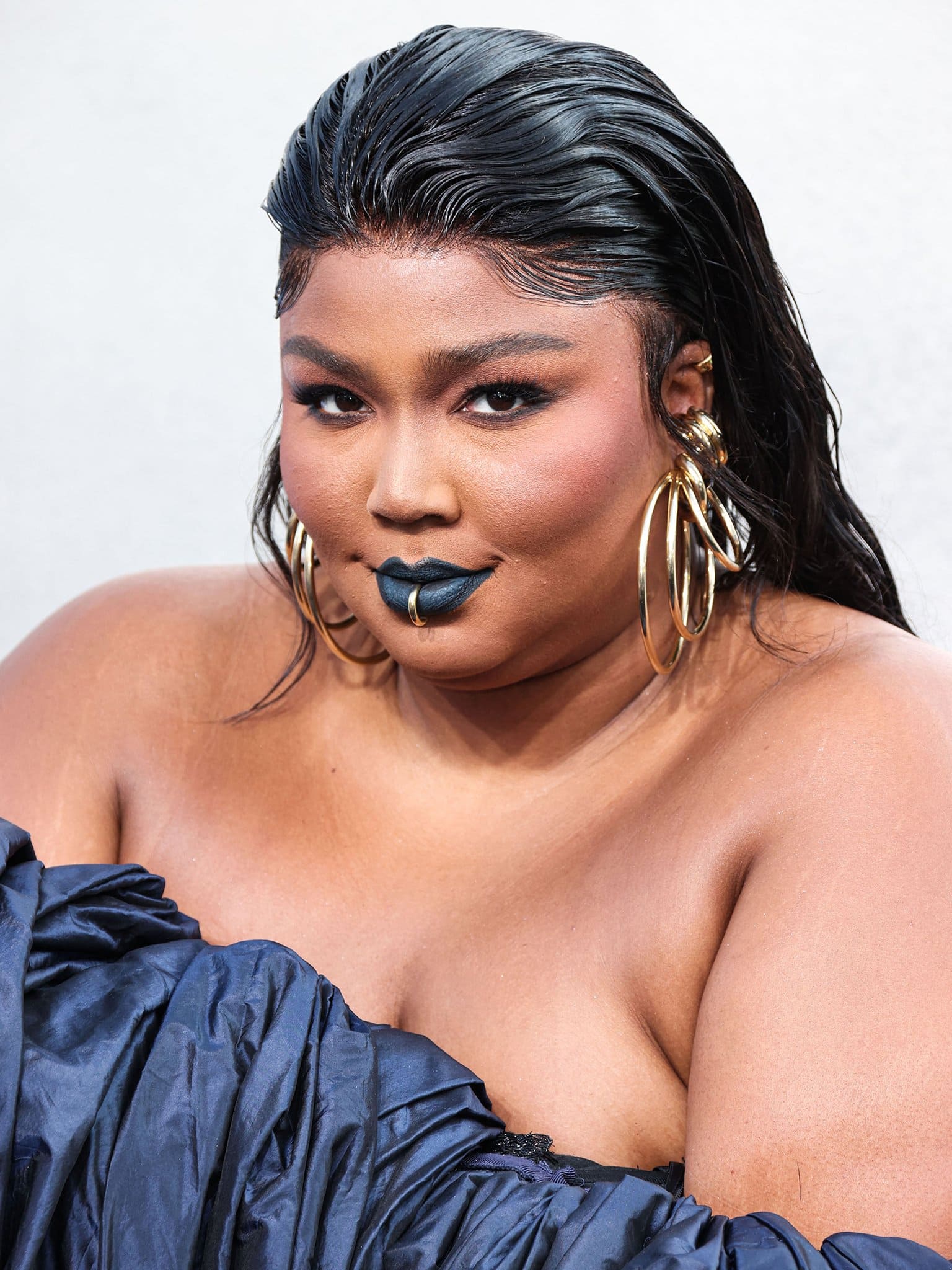 Lizzo finishes off her gothic-glam look with slicked-back wet-look hairstyle and cerulean lipstick