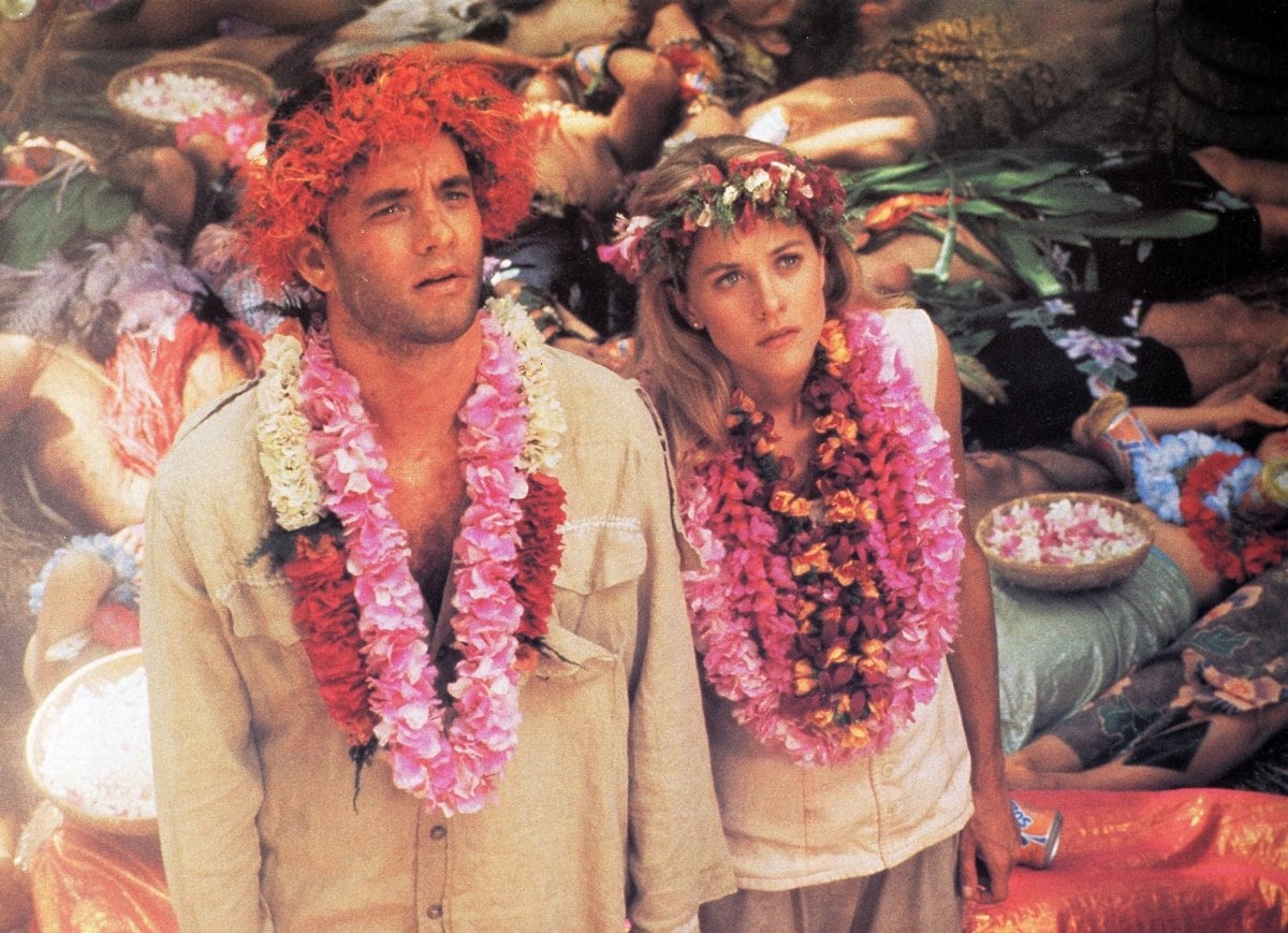Tom Hanks and Meg Ryan, adorned with vibrant floral leis, share a colorful scene in a tropical setting from their quirky romantic comedy Joe Versus the Volcano