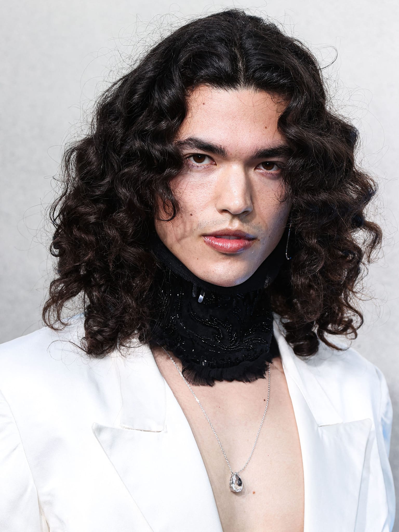 Conan Gray wears his natural curls and styles his look with a Dries Van Noten neckpiece
