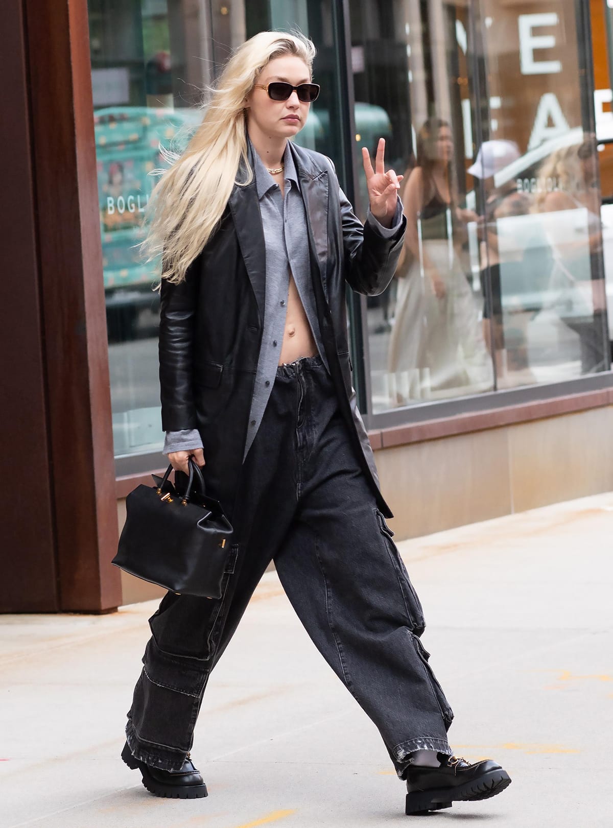 Gigi Hadid flashes her abs in a partially unbuttoned shirt teamed with Zadig & Voltaire leather jacket, cargo jeans, and Gucci loafers