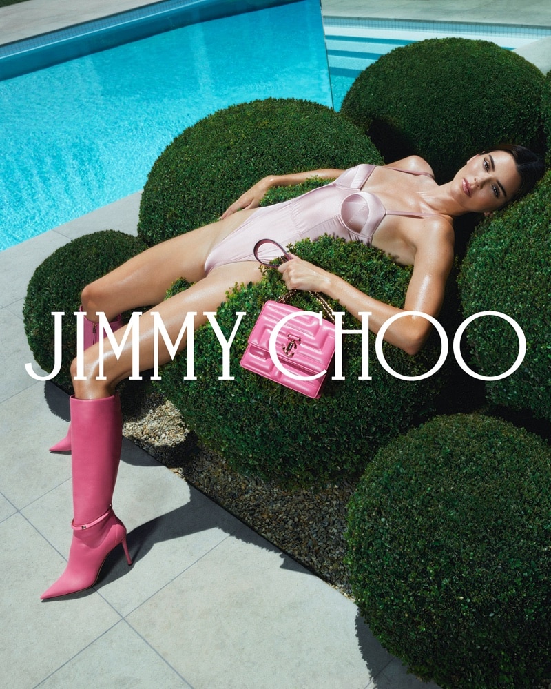 Kendall Jenner posing in a bodysuit with a candy pink handbag and knee-high boots