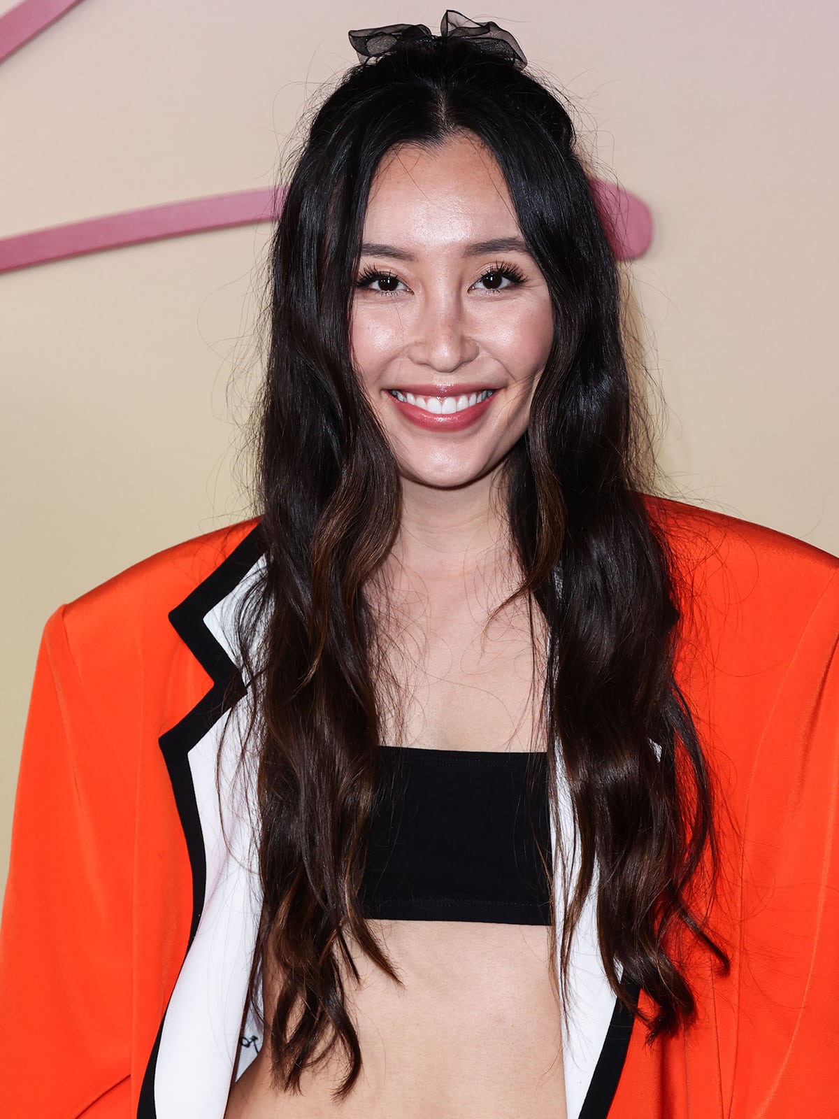 Olivia Sui wears fake lashes and styles her long tresses in a wavy half-up hairstyle with a chiffon bow