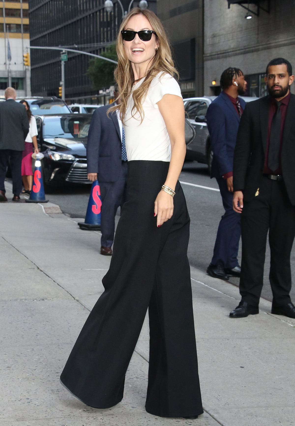 Olivia Wilde pairs a white tee with black wide-leg pants, Casadei platform boots, and Ray-Ban sunnies