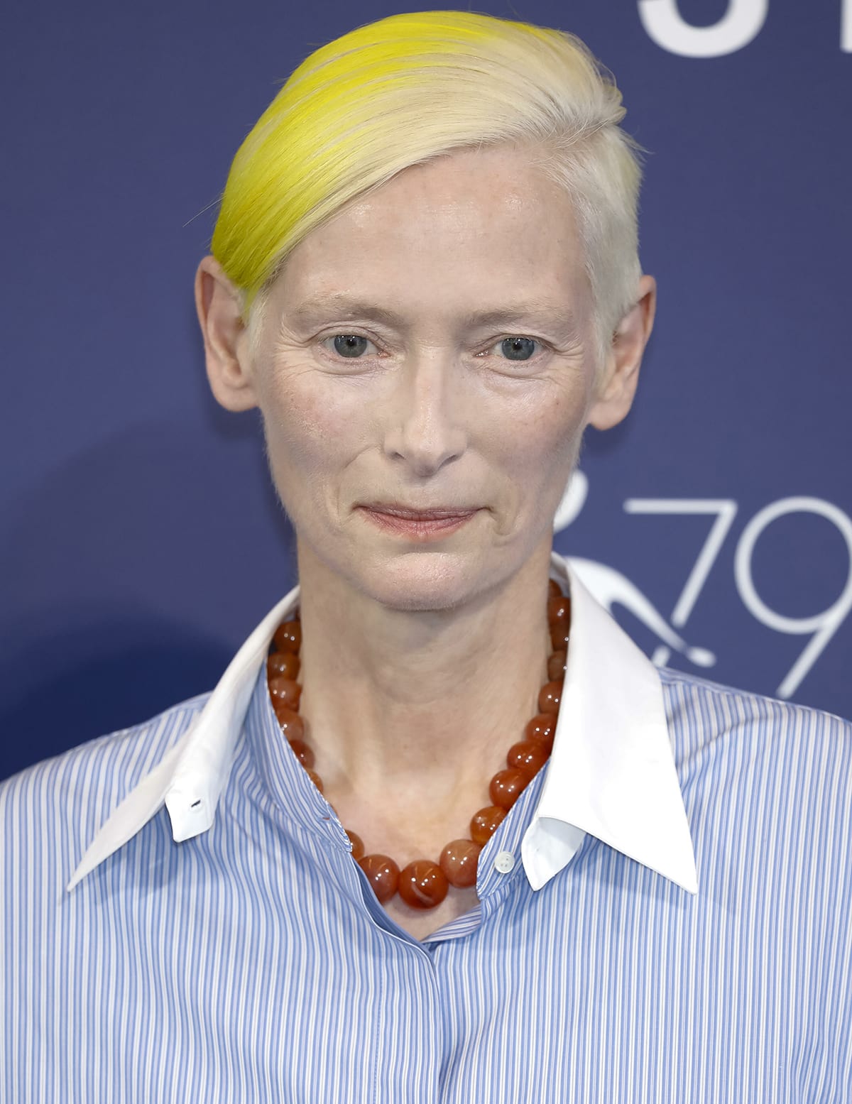 Tilda Swinton styles her Ukraine flag-inspired look with a burnt orange bead necklace, red track pants, and red pumps