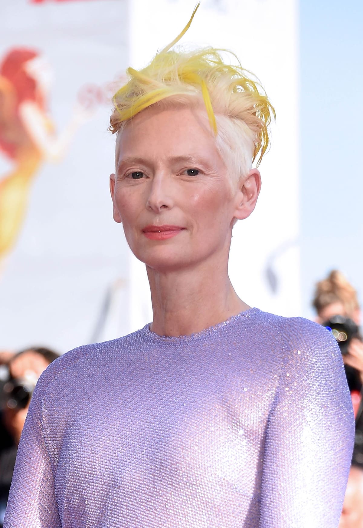 Tilda Swinton styles her yellow hair in a faux hawk and wears peachy pink blush and lipstick