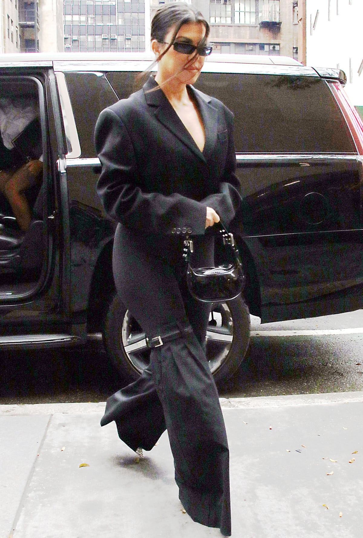 Kourtney Kardashian wearing an oversized blazer with Coperni hybrid flared trousers and a By Far shoulder bag