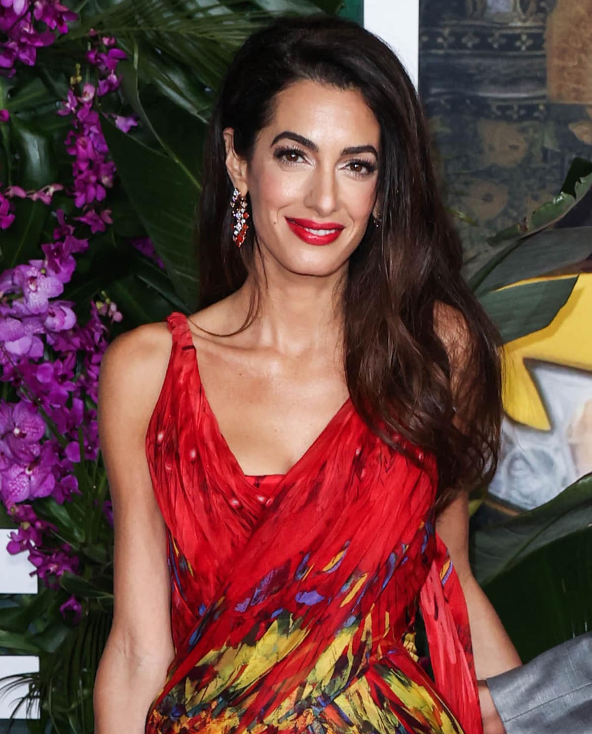 Amal Clooney sweeps her tresses to one side and wears fluttery eyelashes and bright red lipstick