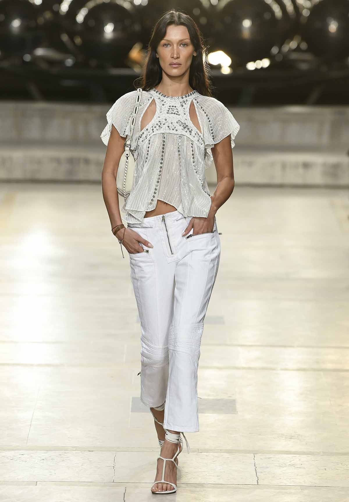 Bella Hadid walks for Isabel Marant in a white cutout top with silver sequins and white pants