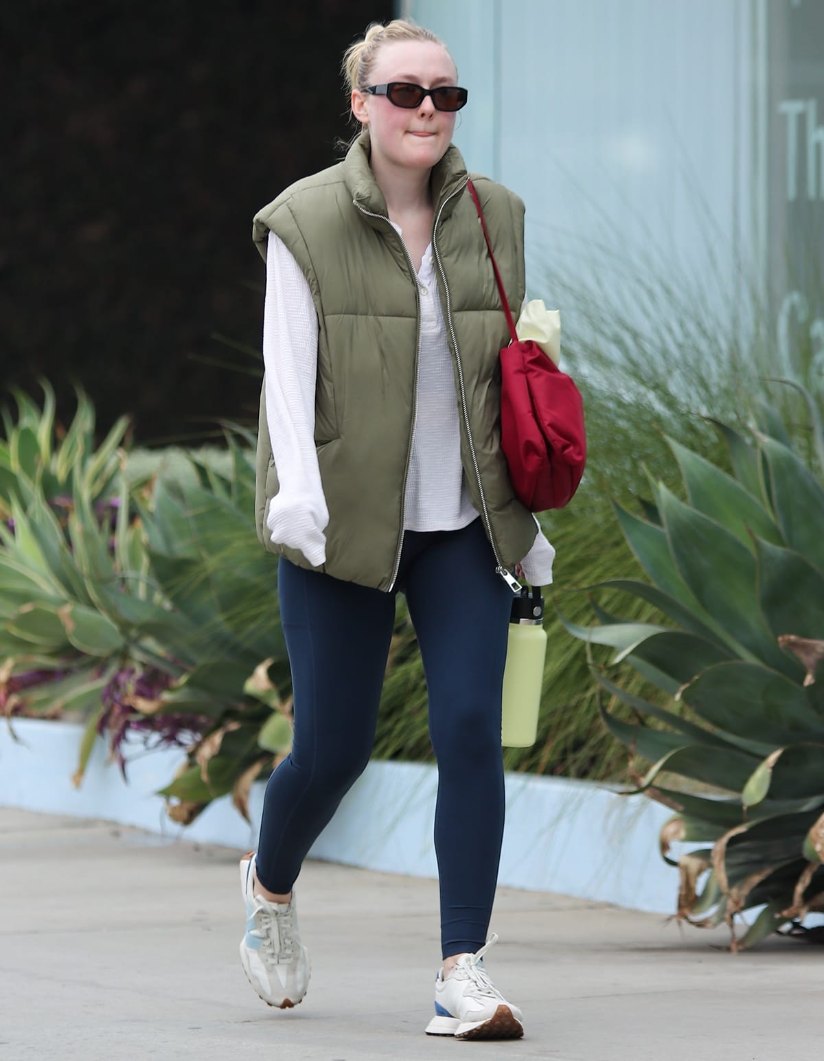 Dakota Fanning in Staud x New Balance 327 “Sea Salt Atlantic” sneakers paired with a khaki vest and navy leggings makes her way to the gym