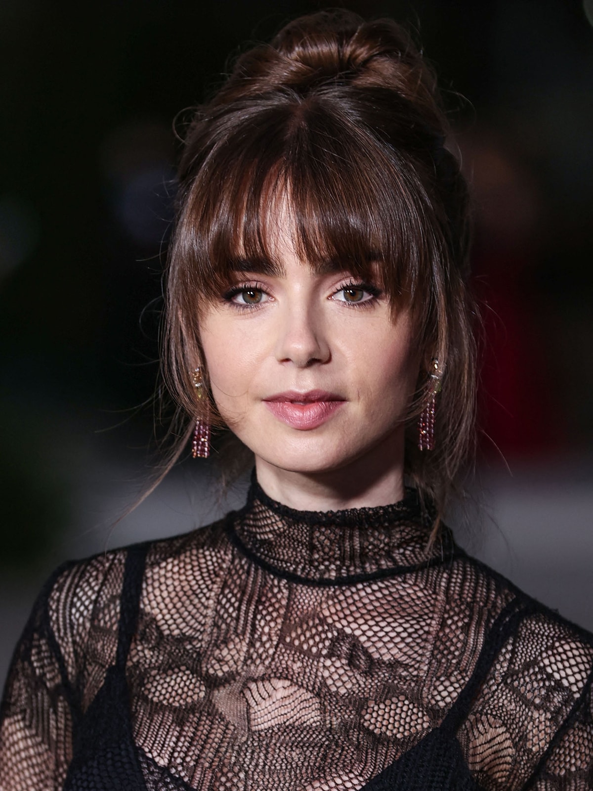 Lily Collins styles her hair in a chic bun with her signature bangs framing her minimally made-up face