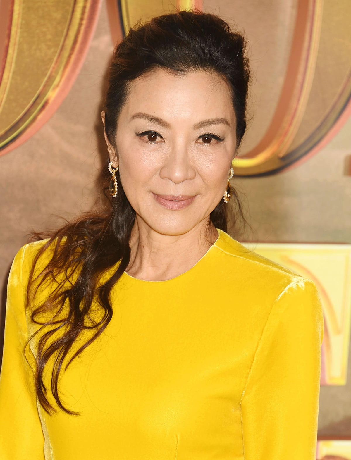 Michelle Yeoh sweeps her tresses into a wavy ponytail and highlights her eyes with cat-eyeliner