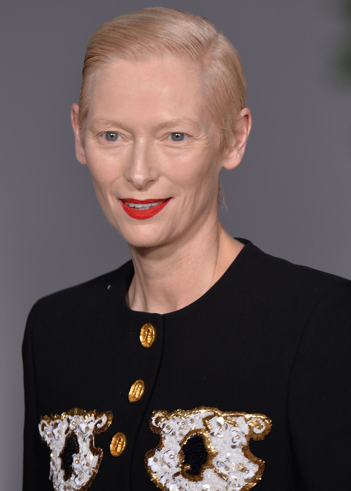 Tilda Swinton wears her signature short hairstyle and adds a pop of color to the look with bright red lipstick