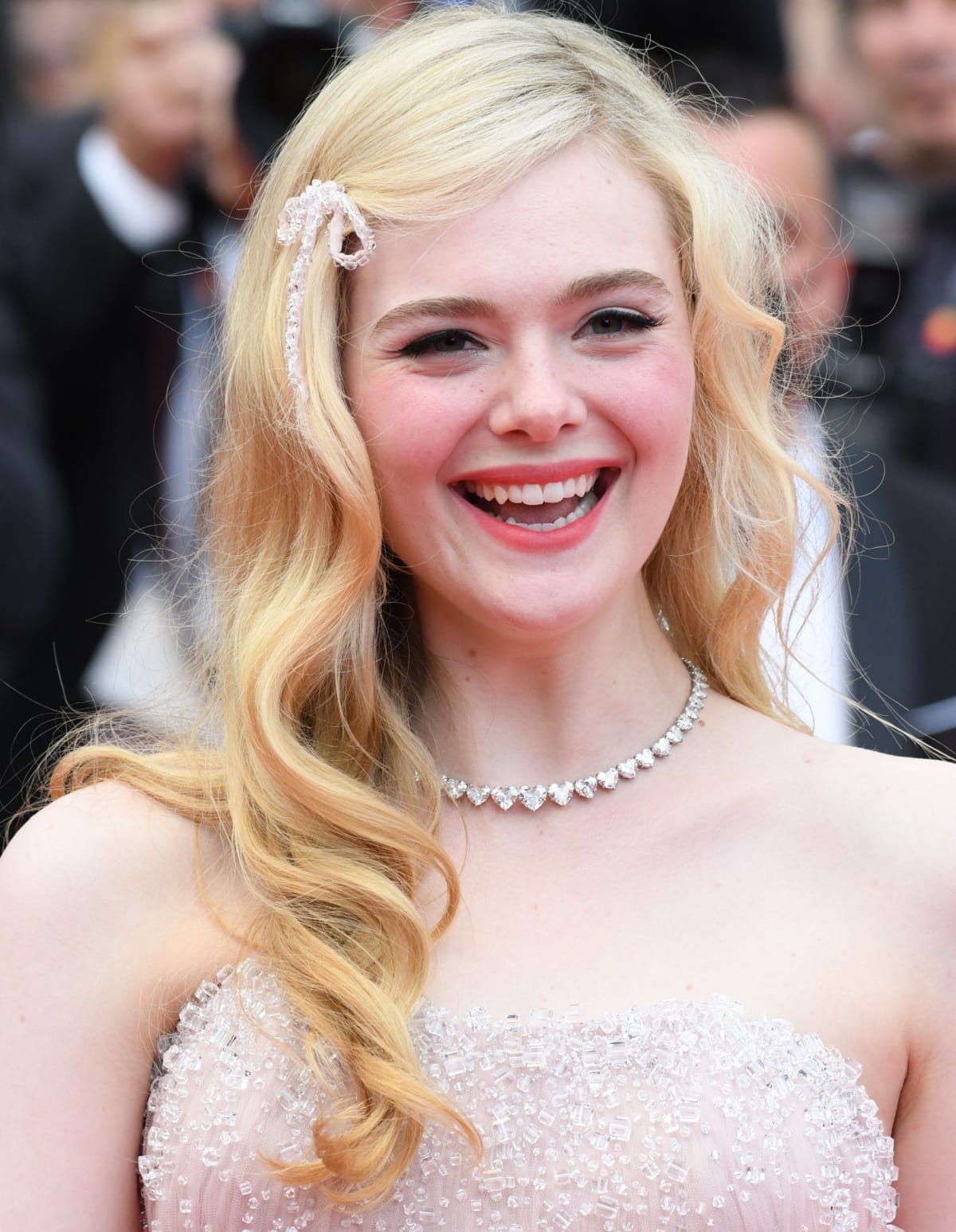 Elle Fanning dazzles on the red carpet in a shimmering beaded gown, complemented by soft waves, a delicate bow hair accessory, and a sparkling diamond necklace