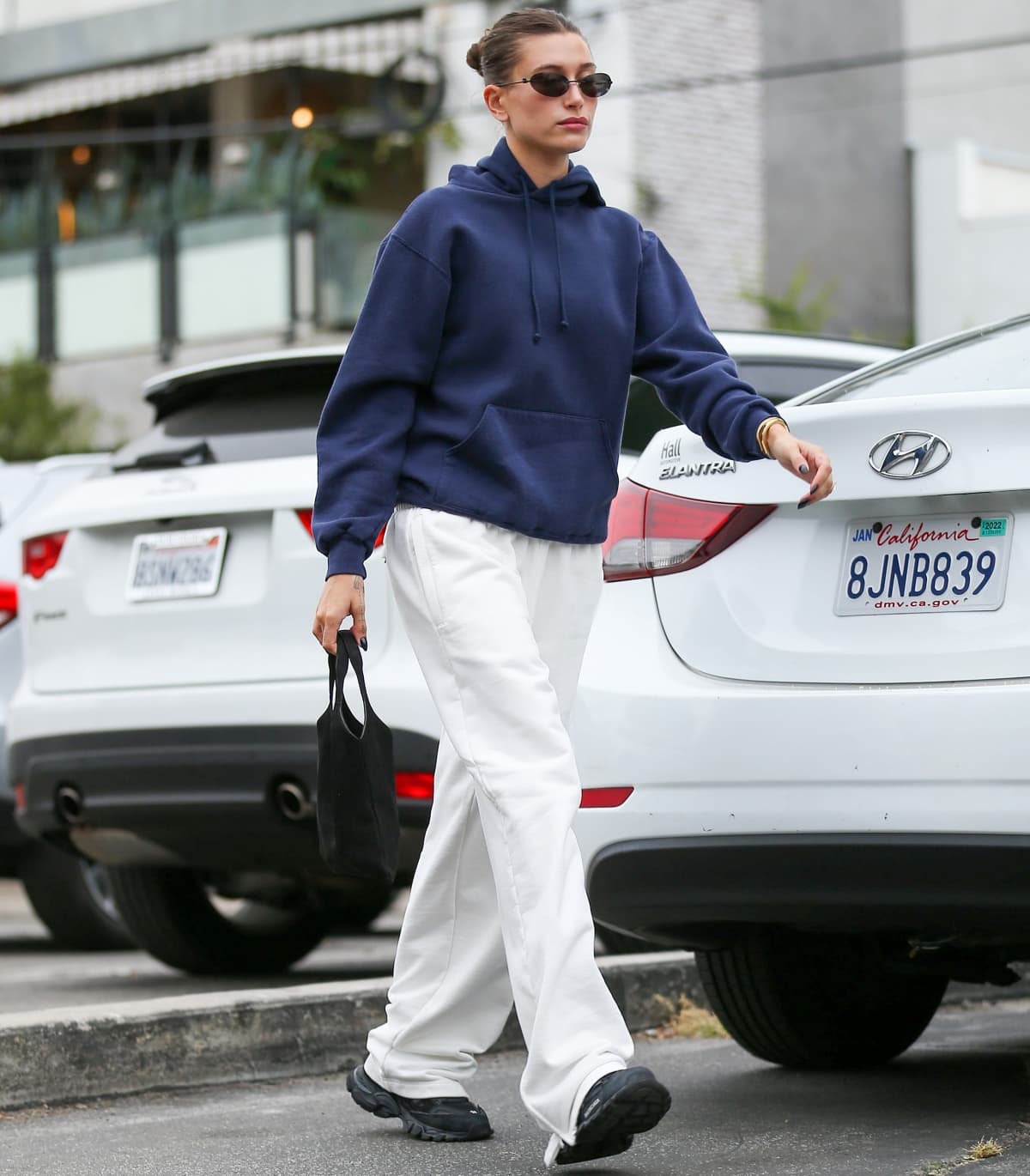 Looking comfy in a blue hooded sweater, white pants, and black sneakers, Hailey Bieber heads to a Pilates class