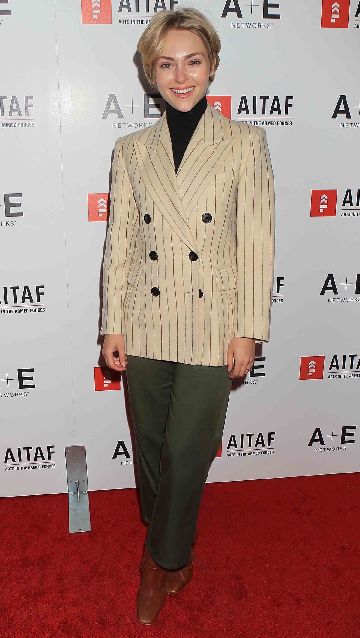 AnnaSophia Robb looks effortlessly chic in a beige pinstripe double-breasted blazer, olive green trousers, and brown pointed-toe boots at the AITAF event