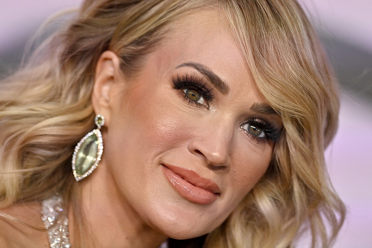 Carrie Underwood styles her blonde hair in side-parted waves and wears heavy mascara with nude lipstick
