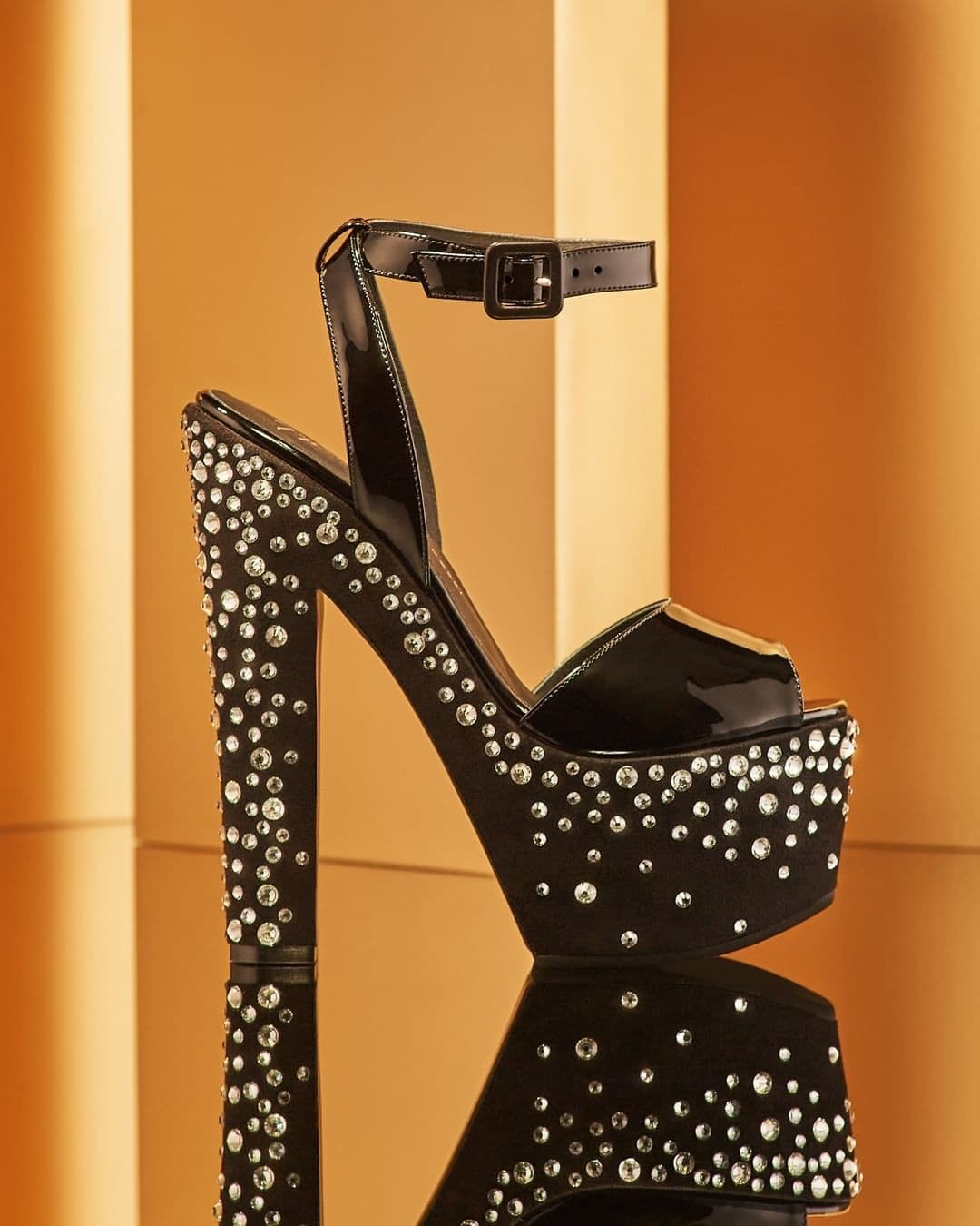 These peep-toe sandals crafted from black patent leather feature a synthetic suede effect fabric-covered bottom, an adjustable ankle strap with an upper-matching small buckle, and a matching chunky platform and heels with crystal-colored rhinestone embroidery