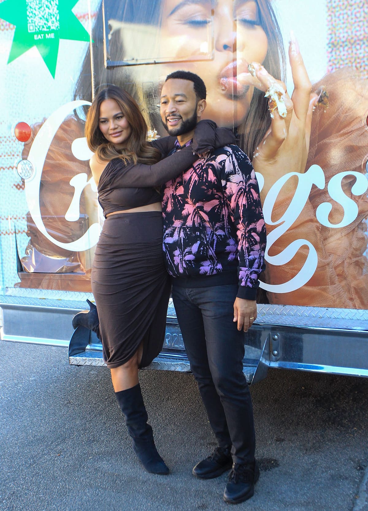 Chrissy Teigen and John Legend posing together in front of the Cravings pop-up food truck in Los Angeles