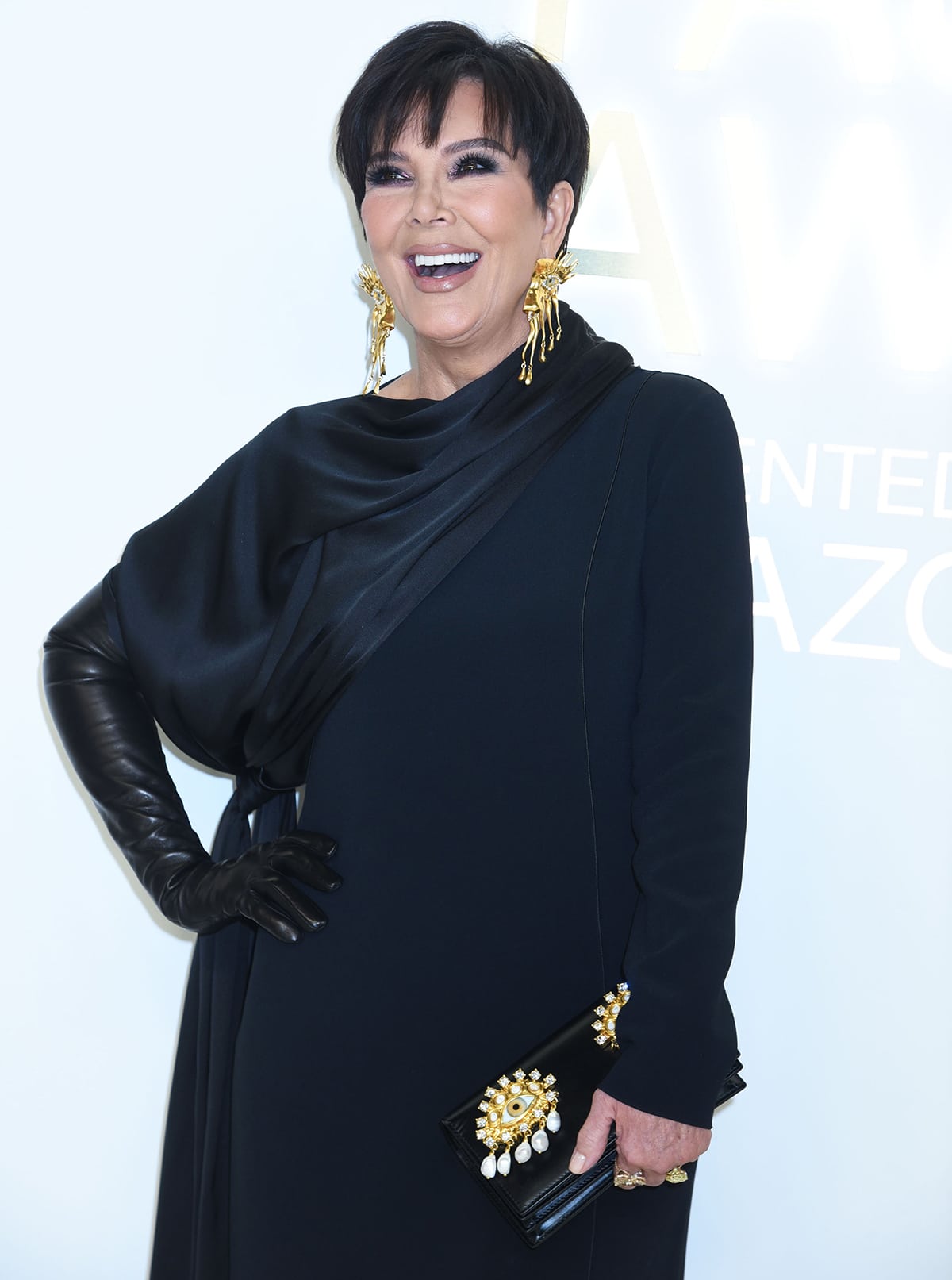 Kris Jenner pairs her black dress with gold accessories, including a pair of Schiaparelli earrings and a matching clutch