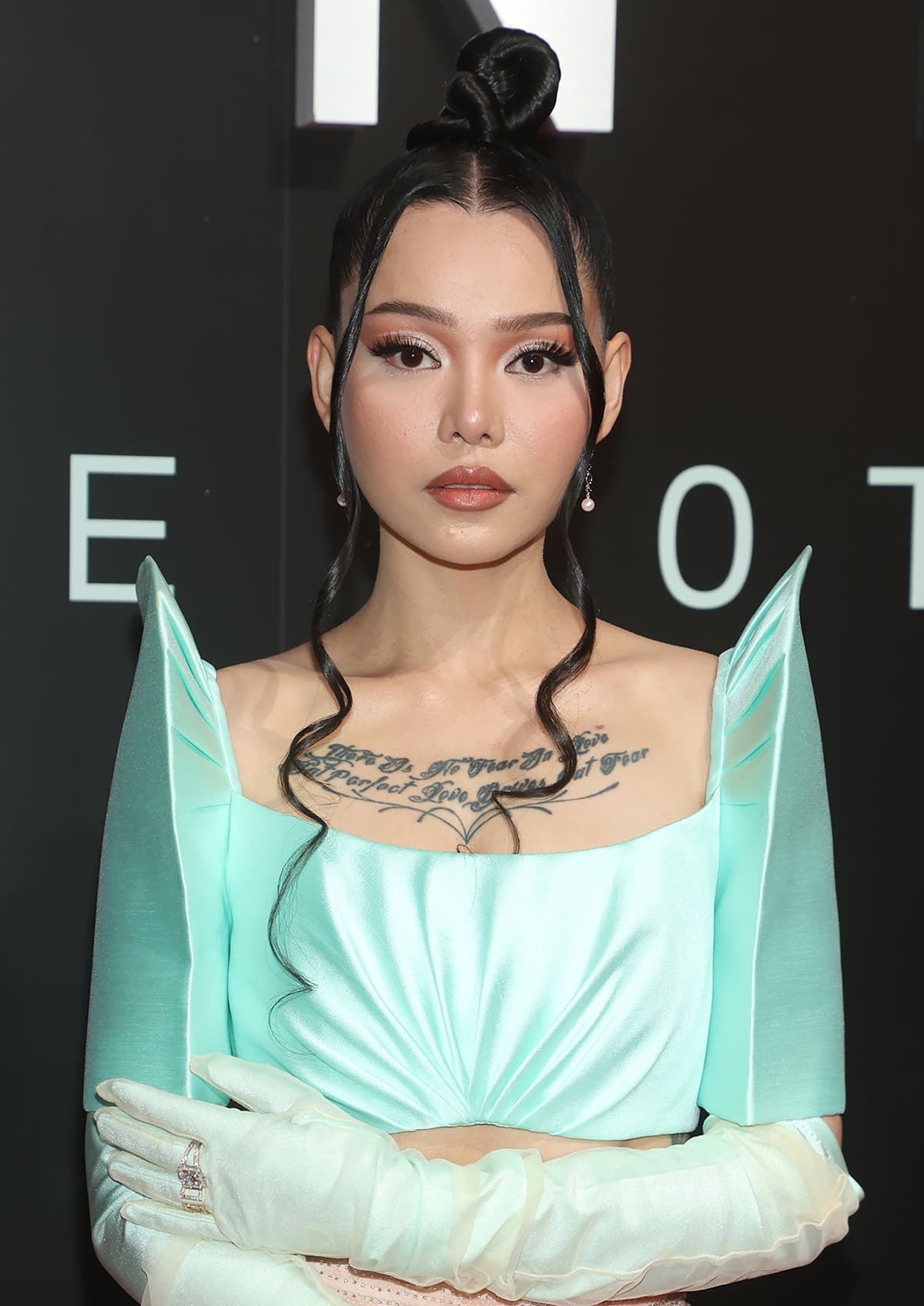 Bella Poarch showcases her chest tattoo and wears her tresses in a top knot with curled tendrils framing her face