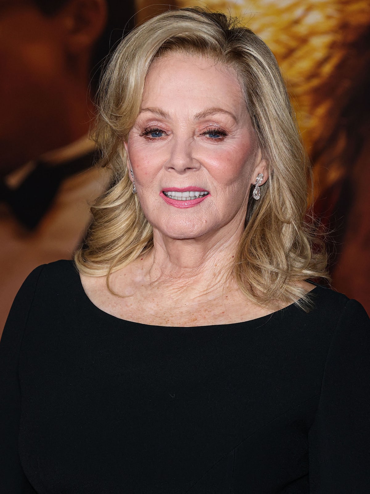 Jean Smart styles her blonde hair in soft waves with a side part and wears soft pink eyeshadow and lipstick