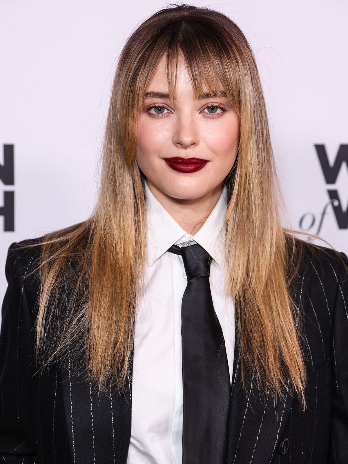 Katherine Langford wears deep mauve lipstick and styles her hair straight with face-framing fringe