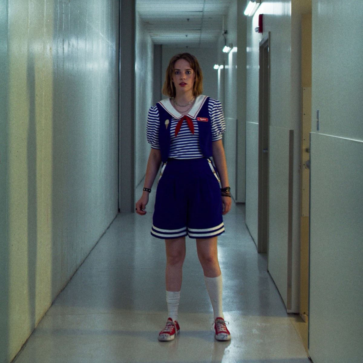 Maya Hawke wears Robin Buckley’s iconic Scoops Ahoy sailor uniform and custom-scribbled red Converse sneakers—personalized with doodles like “boobs”—in Stranger Things Season 3, a look crafted in collaboration with costume designer Amy Parris to subtly reflect the character’s identity and rebellious edge