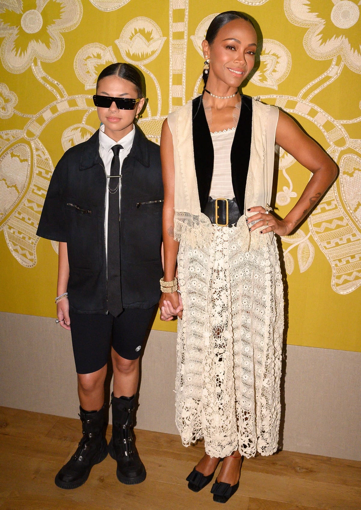 Zoe Saldaña pairs a lace skirt with a velvet-trimmed vest and black bow heels, while holding hands with her niece, who sports a menswear-inspired look at the Dior Haute Couture Fall/Winter 2022-2023 show