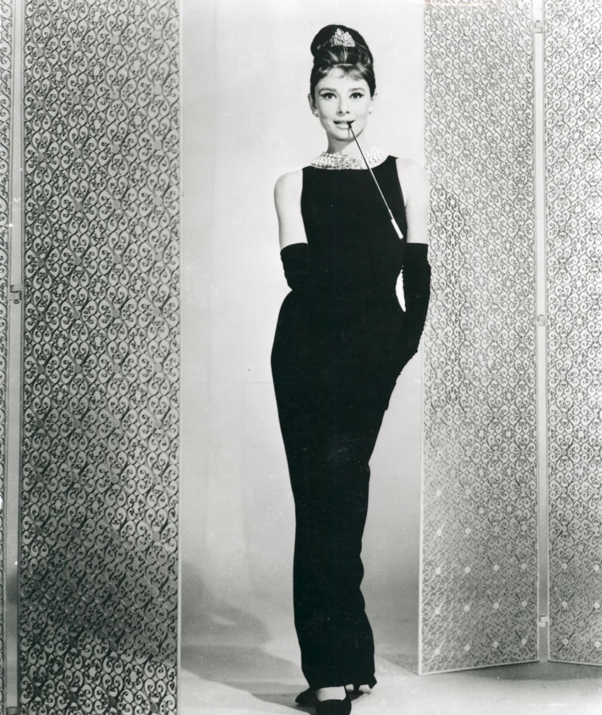 Audrey Hepburn opens Breakfast at Tiffany’s in her legendary black Givenchy column gown, layered pearl necklace, tiara, opera gloves, and black kitten-heel pumps by René Mancini—setting the standard for cinematic elegance