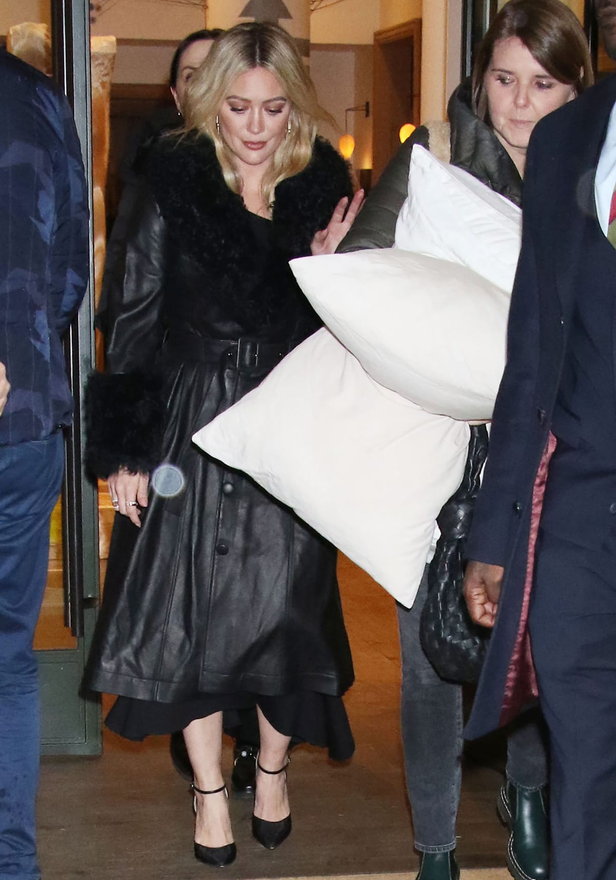 Hilary Duff hides her asymmetrical black dress underneath a black leather coat with fur cuffs and collar