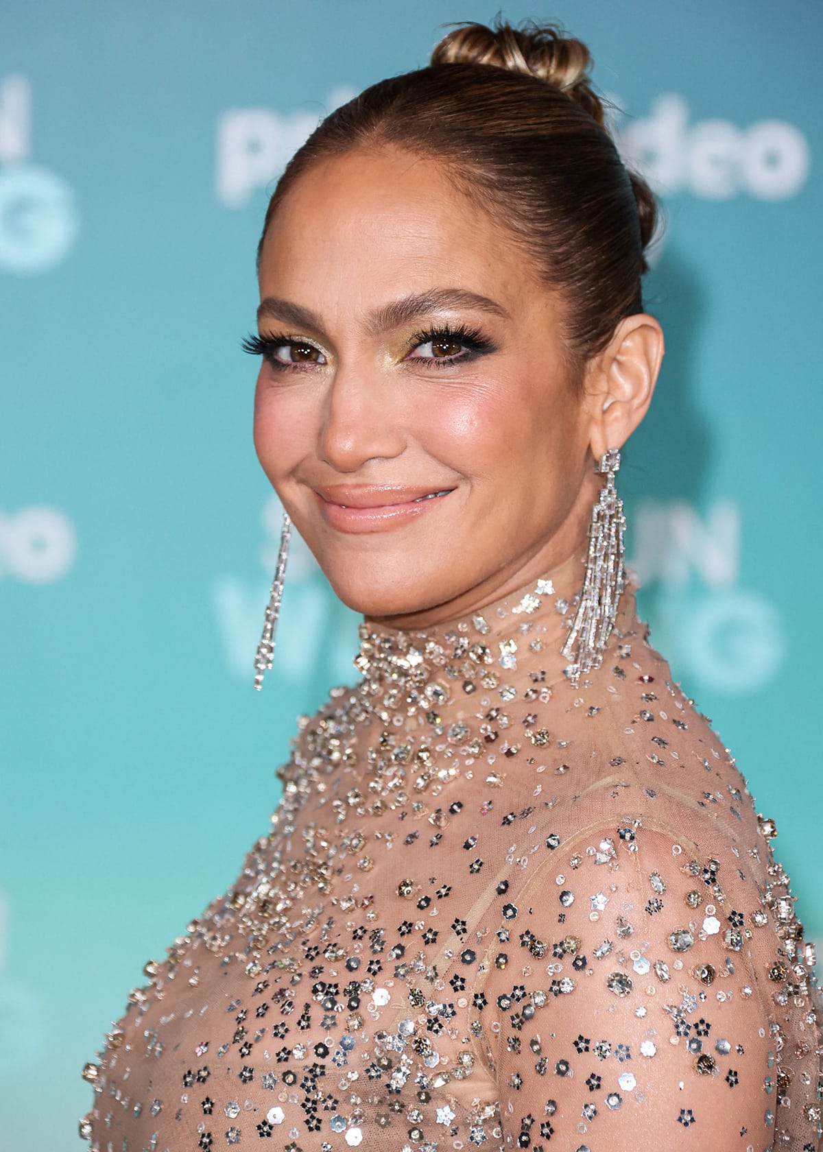 Jennifer Lopez adds more shimmer to her look with Shiphra diamond jewelry and glams up with metallic eyeshadow, false eyelashes, nude lip gloss, and a high bun