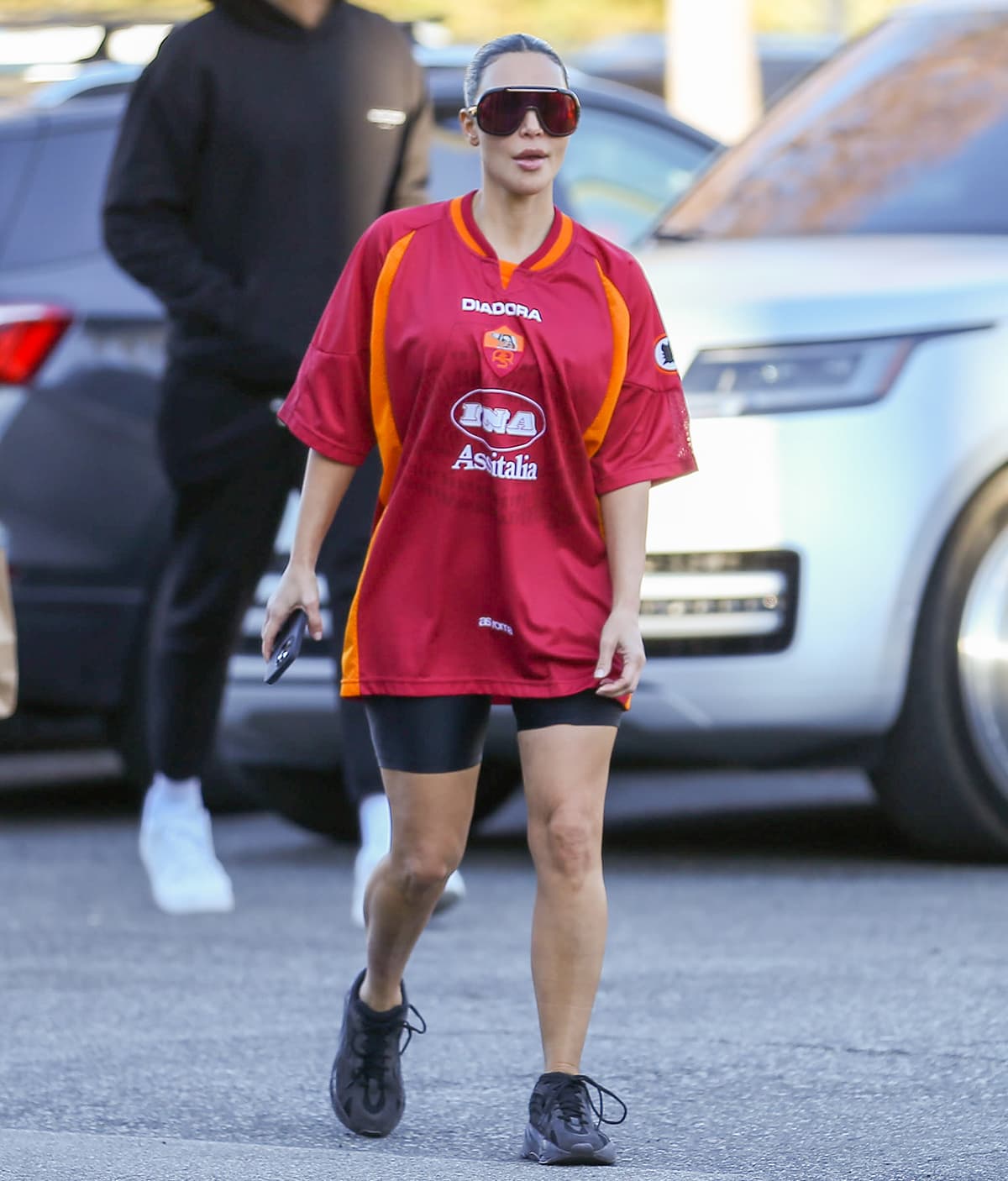 Kim Kardashian keeps a sporty look in a short-sleeved Roma x Diadora jersey top, biker shorts, and Yeezy Boost sneakers