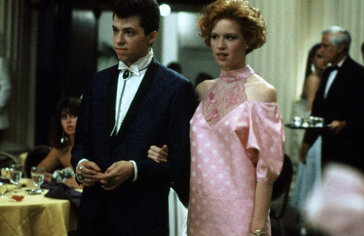Molly Ringwald’s character, Andie, makes a bold DIY fashion statement in Pretty in Pink with her iconic off-shoulder, puffy-sleeved pink polka dot prom dress, crafted from vintage pieces